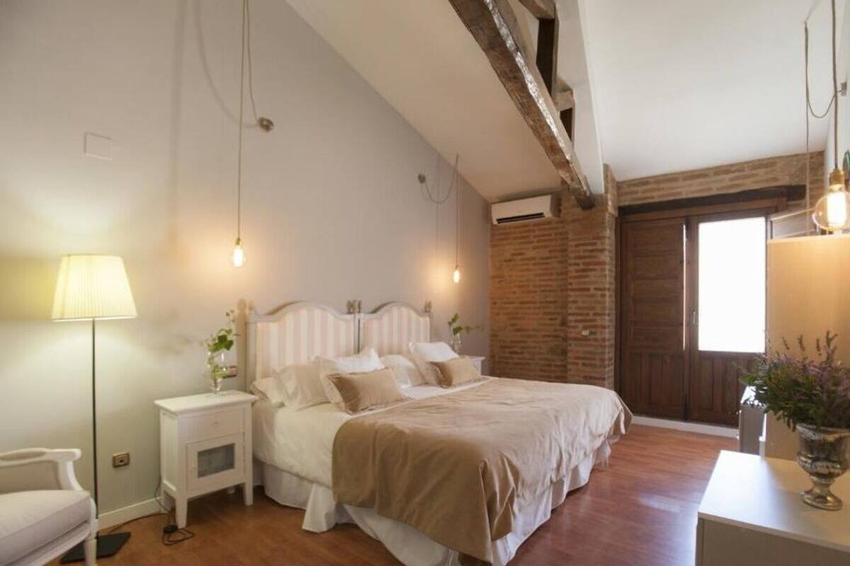 A bedroom with a bed, bedside tables, a lamp, and a brick wall.