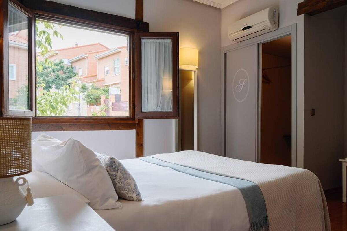 A bedroom with a bed, a bedside table, an air conditioning unit, and a window with curtains.