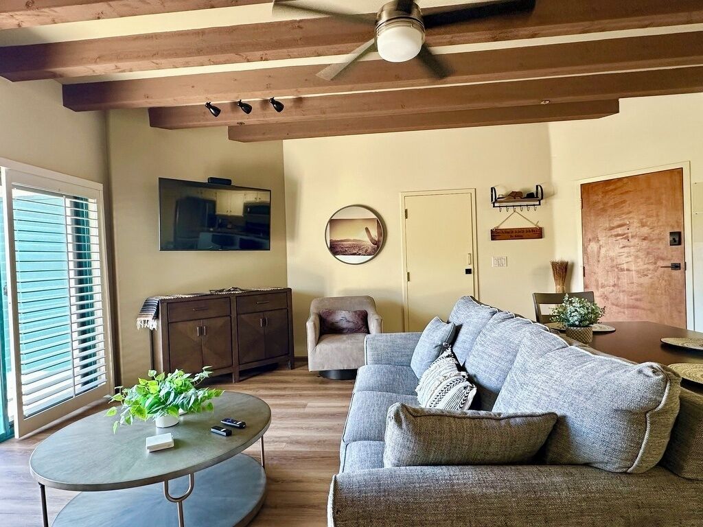 Un salon avec un canapé, une table basse, un ventilateur de plafond, un téléviseur et une porte.