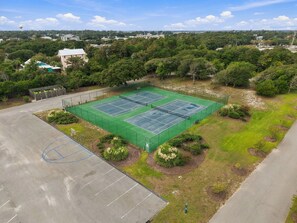 A tennis court surrounded by greenery and a parking area. - Welcome to Sound of the Sea 102N (Emerald Isle)