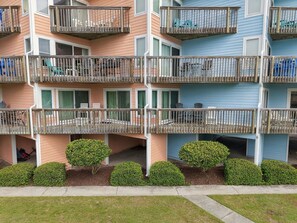 A multi-story residential building with balconies, a lawn, and a row of bushes. - Welcome to Sound of the Sea 102N (Emerald Isle)