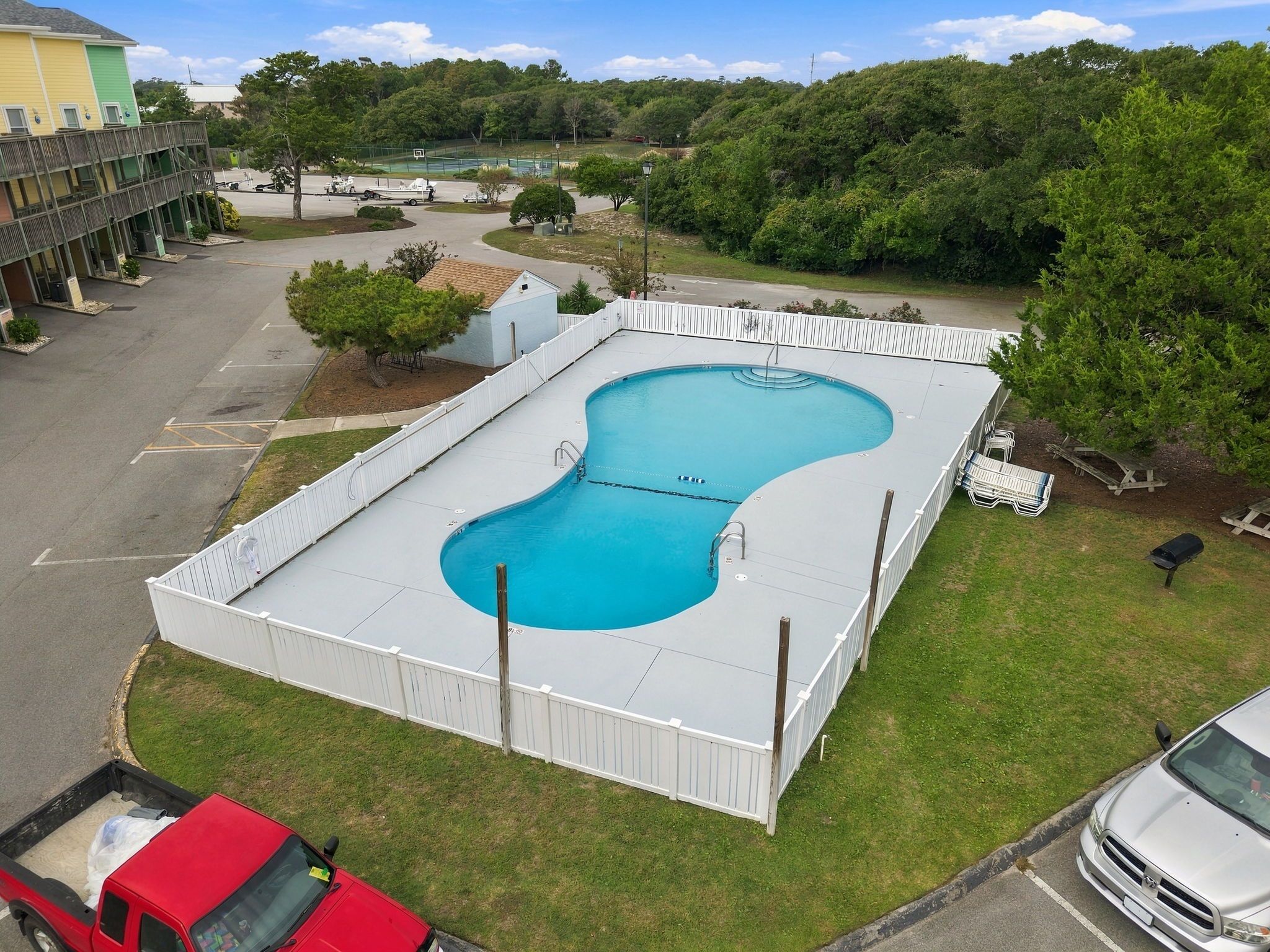 A swimming pool with a white fence, surrounded by grass and trees.