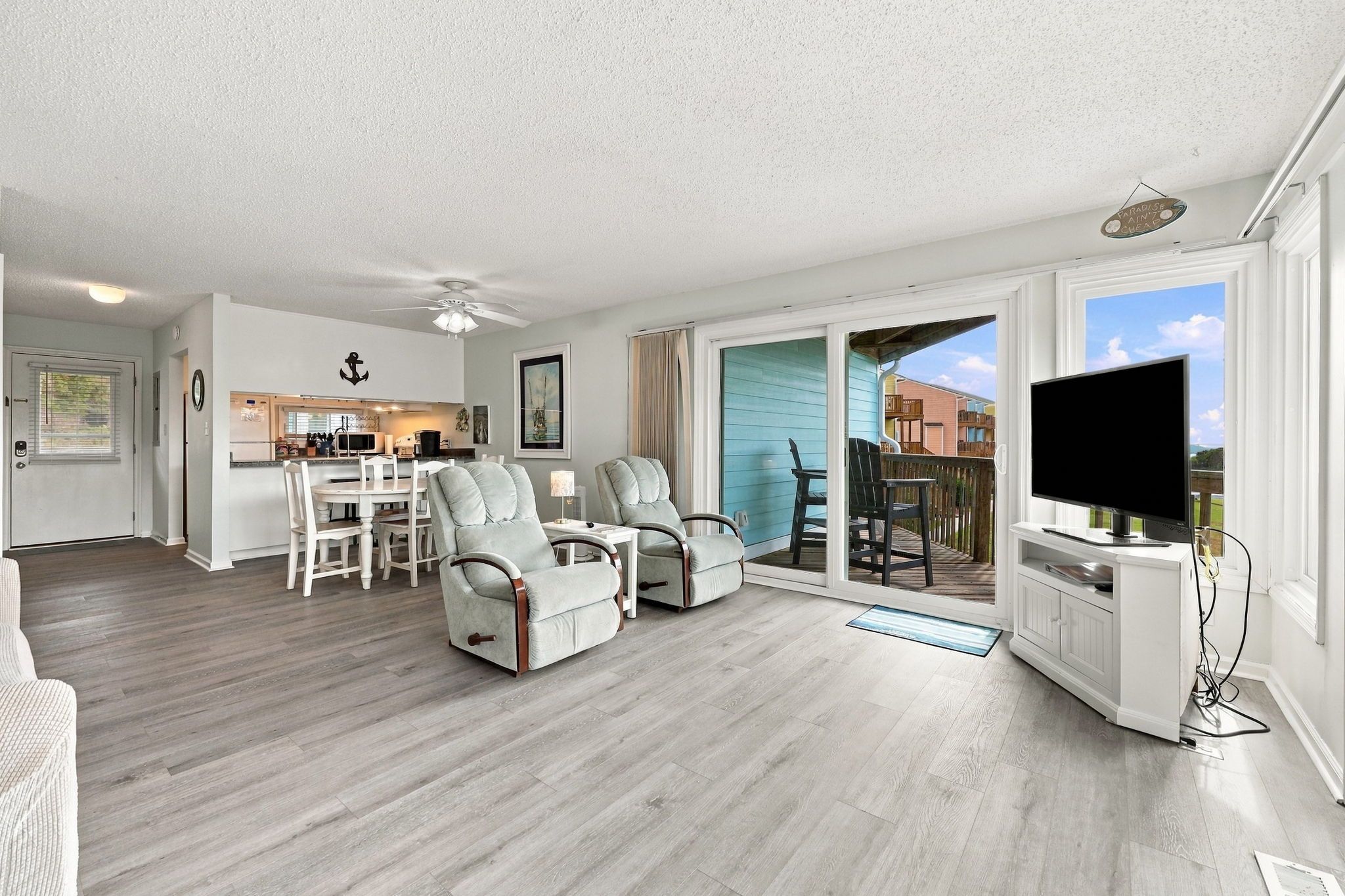 A spacious living area with a sliding glass door leading to a balcony, a flat-screen TV, and a ceiling fan.