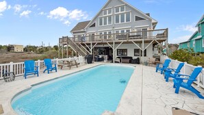Una casa a due piani con piscina, sedie blu e un patio.