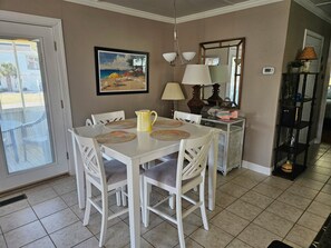 A dining area with a white table, chairs, a pitcher, and a beach-themed painting on the wall.