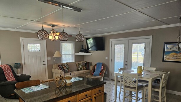 A kitchen with a central island, wooden cabinets, a dining area with a table and chairs, a sofa, and a television mounted on the wall.
