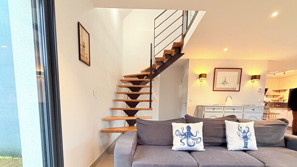 Una sala moderna con una mesa de centro de madera, un sofá gris y una escalera que sube a un nivel superior.