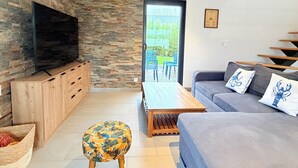 Una sala de estar moderna con una pared de piedra, un televisor de pantalla plana, un sofá gris, una mesa de centro de madera y un otoman con estampado.