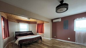 Un dormitorio con cama, piso de madera, ventilador de techo y aire acondicionado.