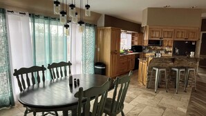 Un comedor con mesa y sillas de madera, una cocina con armarios de madera y una zona de bar con taburetes.