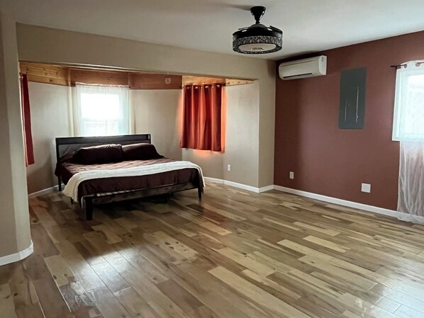 Un dormitorio con cama, piso de madera, ventilador de techo y aire acondicionado.