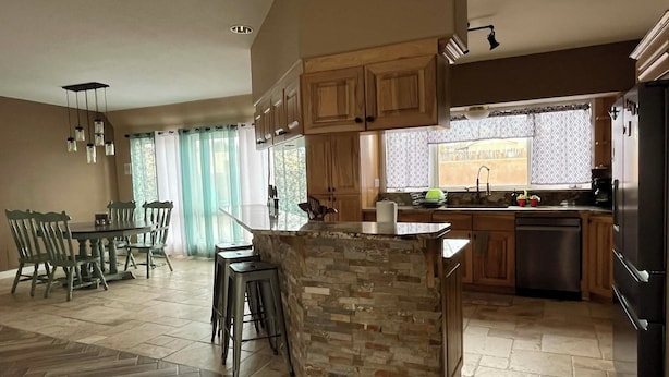 Una cocina moderna con armarios de madera, una isla de piedra y un comedor con sillas.