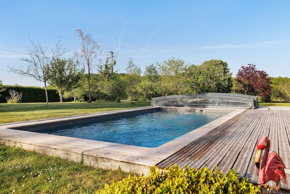 Ein Schwimmbecken mit Holzterrasse, umgeben von Grünpflanzen und Bäumen.