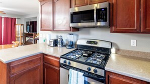 A kitchen with wooden cabinets, a stainless steel stove, a microwave, and a granite countertop.