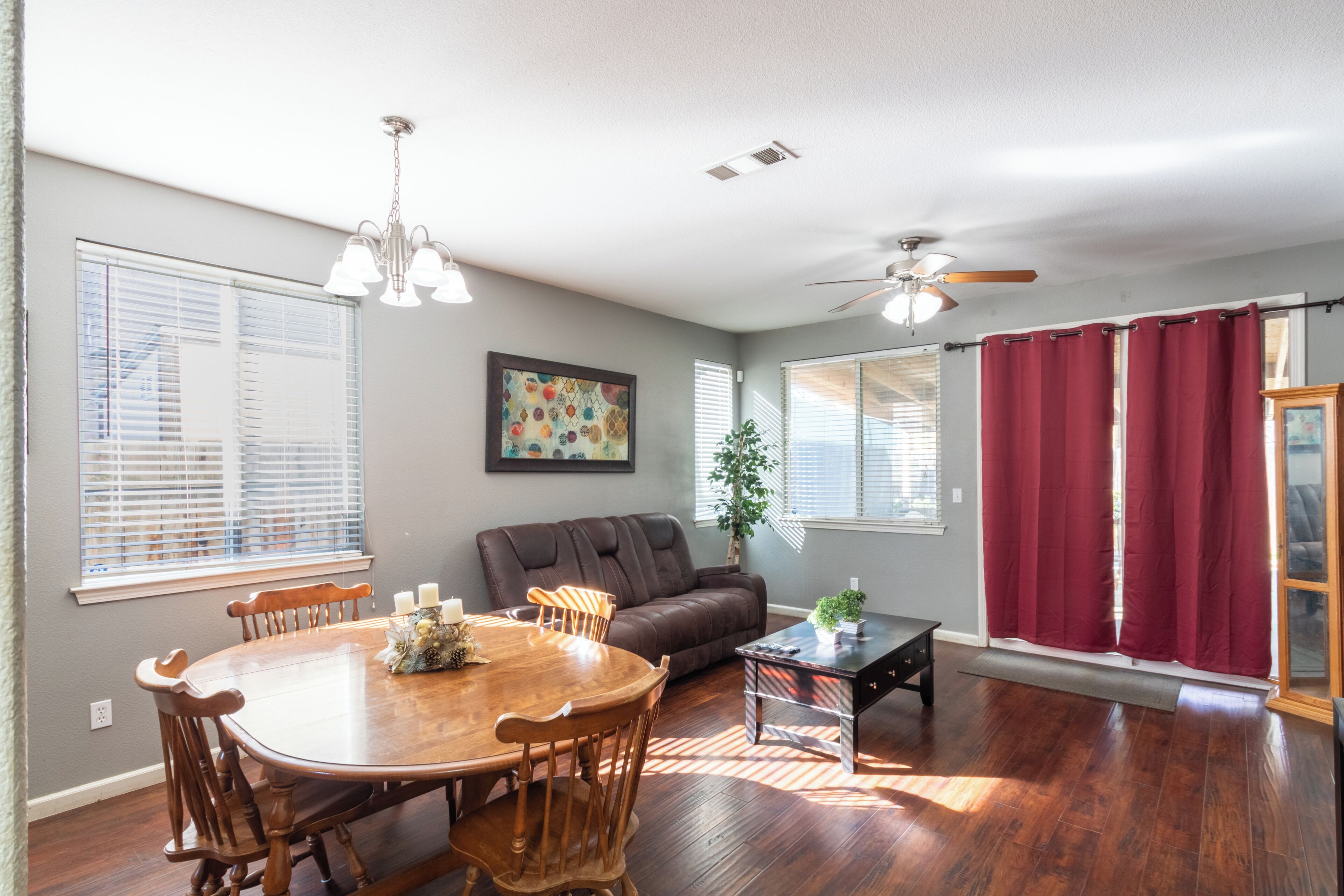 A dining area with a wooden table and chairs, a brown sofa, a ceiling fan, and a window with blinds.