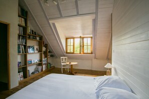 A bedroom with a sloped ceiling, a bed, a small table, a chair, and a bookshelf. - Guest Room "Moulin Du Tourous - Room 1" with Shared Terrace, Garden, and Wi-Fi (Plouédern)