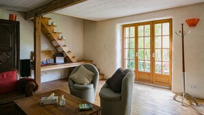 Une pièce avec un escalier en bois, un canapé, une table avec un boîte de mouchoirs et un livre, et une fenêtre donnant sur un paysage verdoyant.
