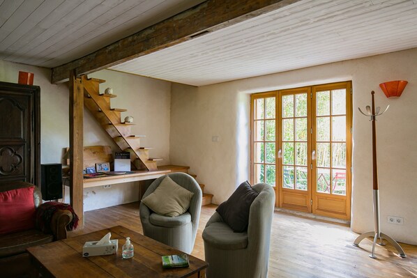 Une pièce avec un escalier en bois, un canapé, une table avec un boîte de mouchoirs et un livre, et une fenêtre donnant sur un paysage verdoyant.