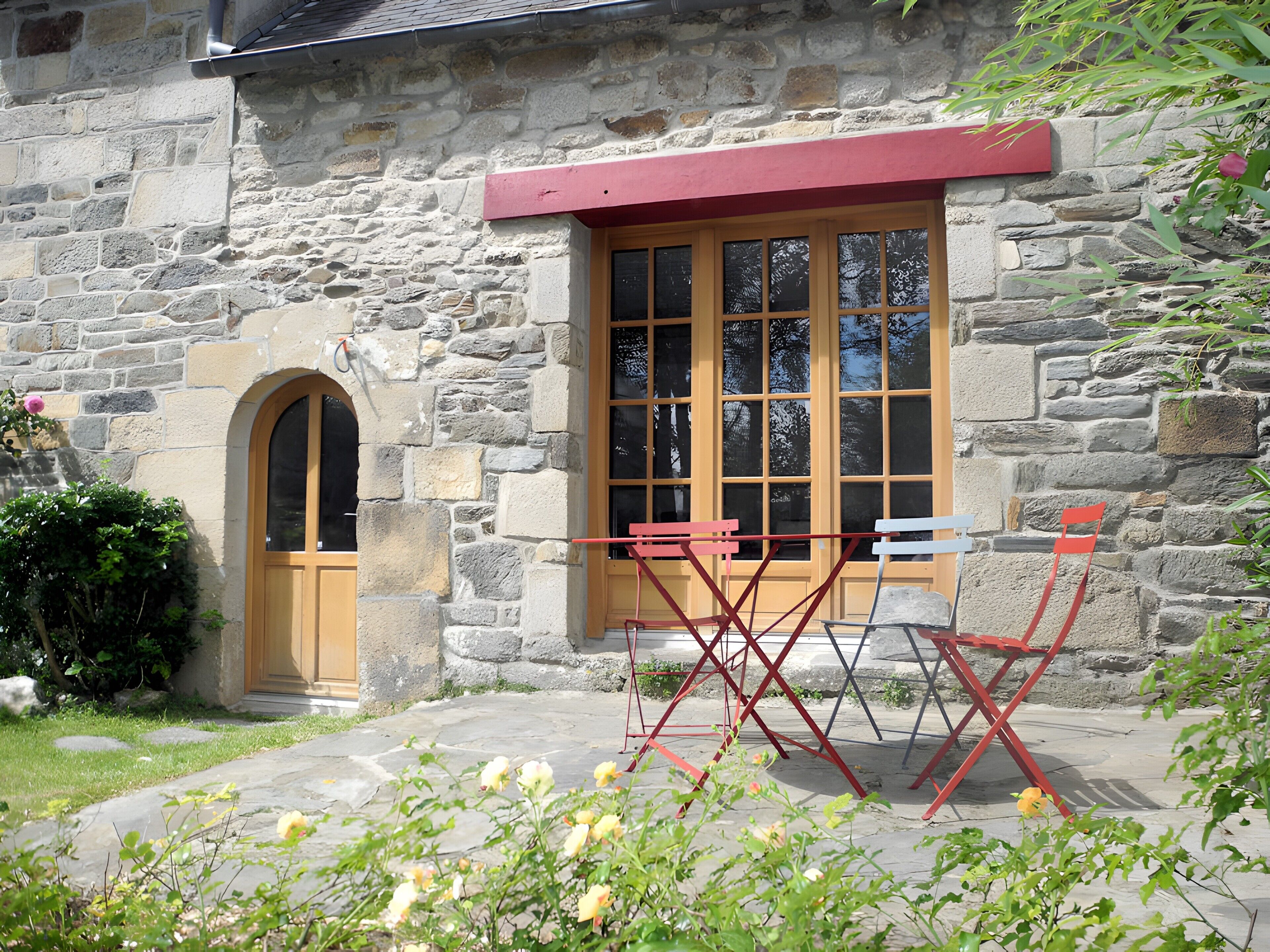 A stone building with a wooden door and windows, a red bench, and a small garden area.