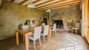 Une salle à manger rustique avec une table en bois, des chaises, un mur en pierre et une cheminée.