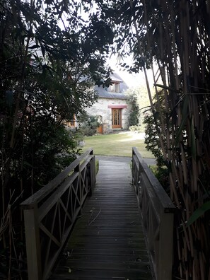 A wooden bridge leading to a stone house with a red door and a small garden. - Guest Room "Moulin Du Tourous - Room 1" with Shared Terrace, Garden, and Wi-Fi (Plouédern)