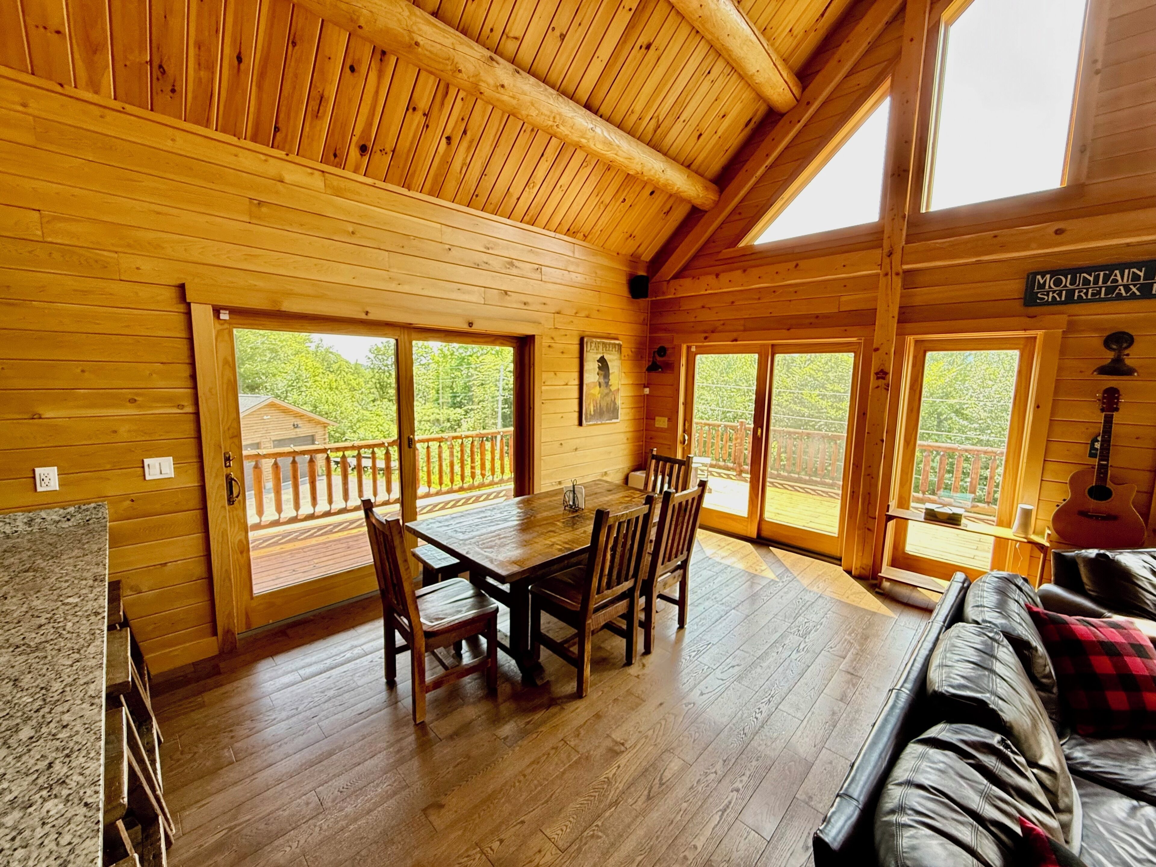 A wooden cabin interior with a dining area, a couch, and a guitar.