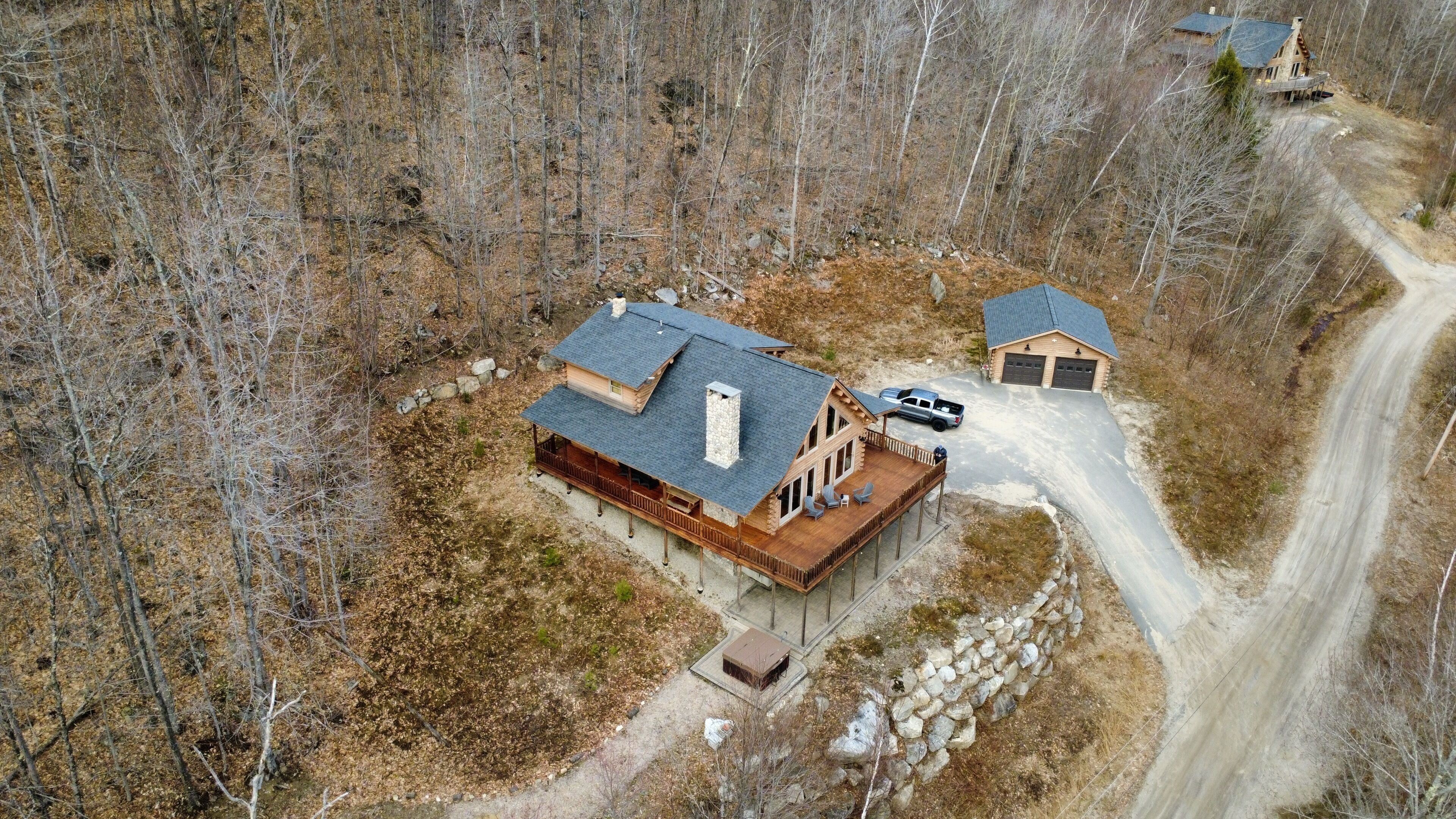 A cabin with a large deck, a garage, and a dirt road leading to it.
