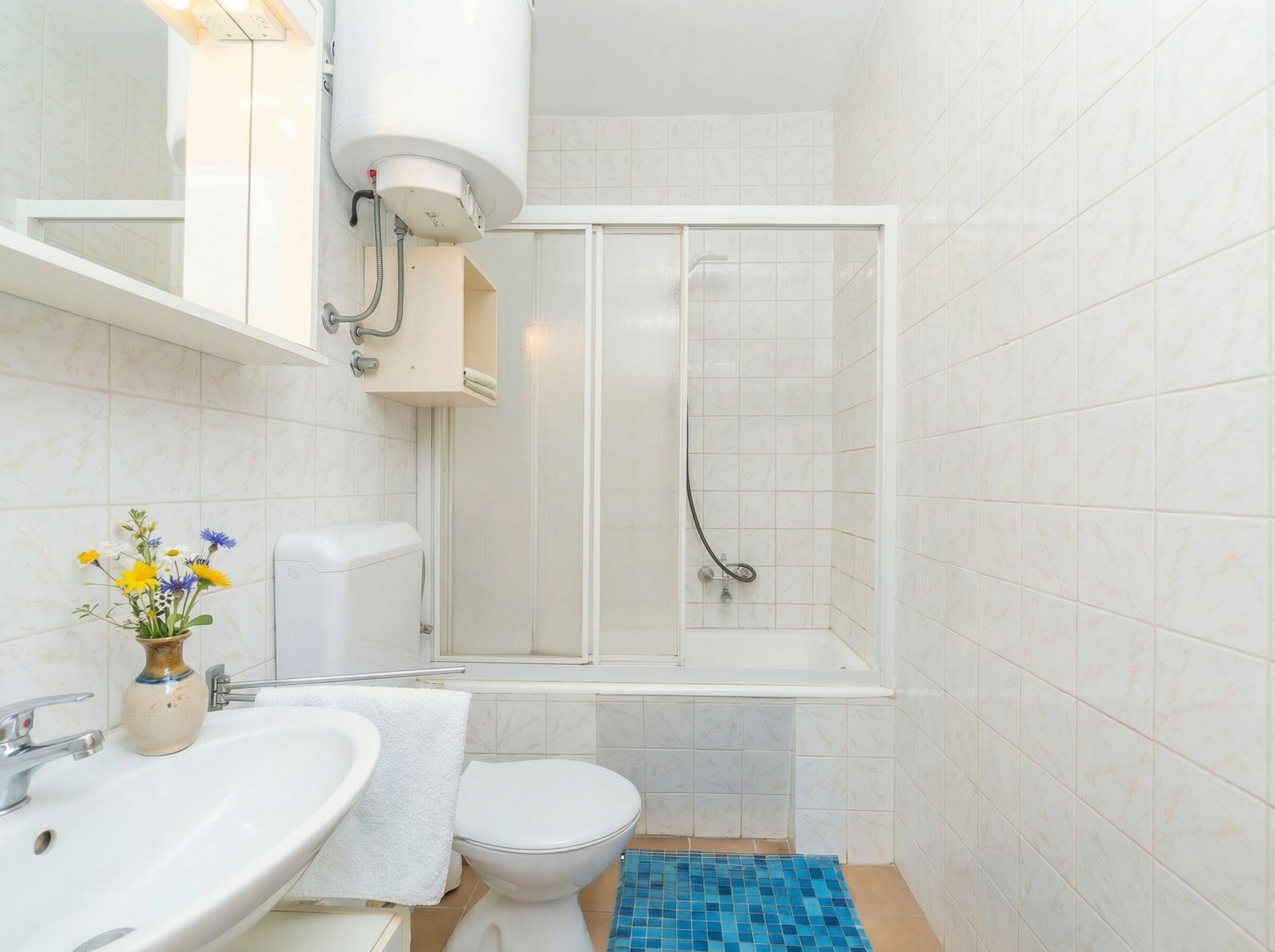Ein Badezimmer mit Toilette, Waschbecken, Dusche und einer kleinen Vase mit Blumen.