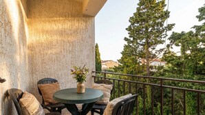 Un balcon avec une table ronde et des chaises, un vase rempli de fleurs et une vue sur la verdure et les bâtiments.