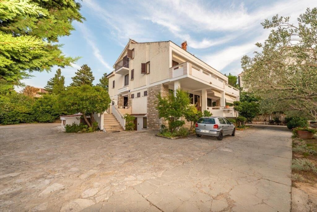 Une maison à deux étages avec une façade en pierre, une voiture garée dans l’allée et un petit jardin.