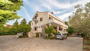 Une maison à deux étages avec une façade en pierre, une voiture garée dans l’allée et un petit jardin.