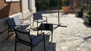 En udendørs terrasse med et bord, stole og en stor parasol, samt en bygning i baggrunden.