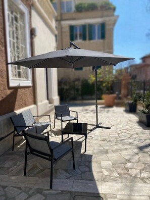 An outdoor patio with a table and chairs, a large umbrella, and a building in the background. - GH Villa Poerio   Deluxe Double Room (ROMA)
