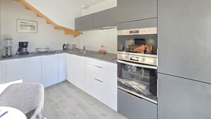 Una cuina moderna amb armaris blancs, forn encastrat i cafetera.