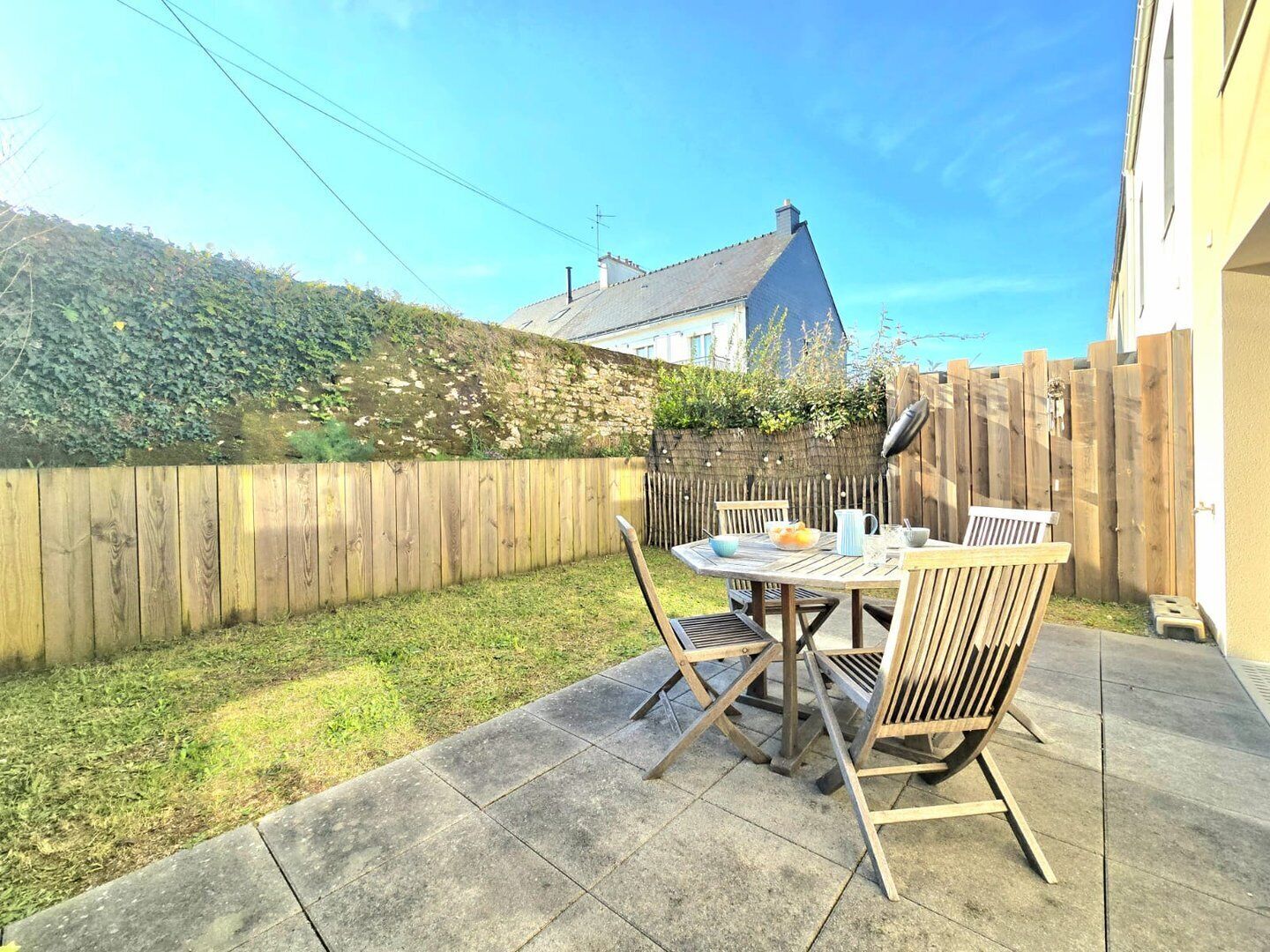 A patio with a table and chairs, a wooden fence, and a house in the background.
