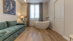A modern bathroom with a freestanding bathtub, a green sofa, and a painting of a bird on the wall. - GH Villa Poerio   Quadruple Room with Bath (ROMA)