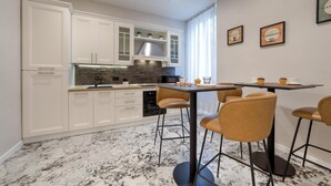 A modern kitchen with white cabinets, a black countertop, and a dining area with two chairs and a table. - GH Villa Poerio   Quadruple Room with Bath (ROMA)