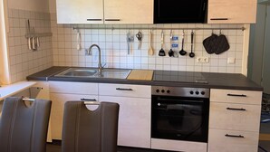 Une cuisine compacte équipée d’un évier, d’une cuisinière, d’un four et d’ustensiles suspendus.