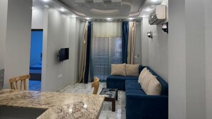 A modern living room with a sofa, a dining table, and a TV mounted on the wall. - Two bedroom apartment with Swimming Pool in the Intercontinental area, Hurghada (Red Sea Governorate)