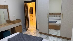 A bedroom with a bed, a wardrobe, a mirror, and a door leading to a bathroom. - Two bedroom apartment with Swimming Pool in the Intercontinental area, Hurghada (Red Sea Governorate)