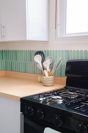 A kitchen with a stove, a window, and a green backsplash.