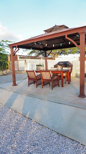 An outdoor patio with a pergola, a table, chairs, and a grill.