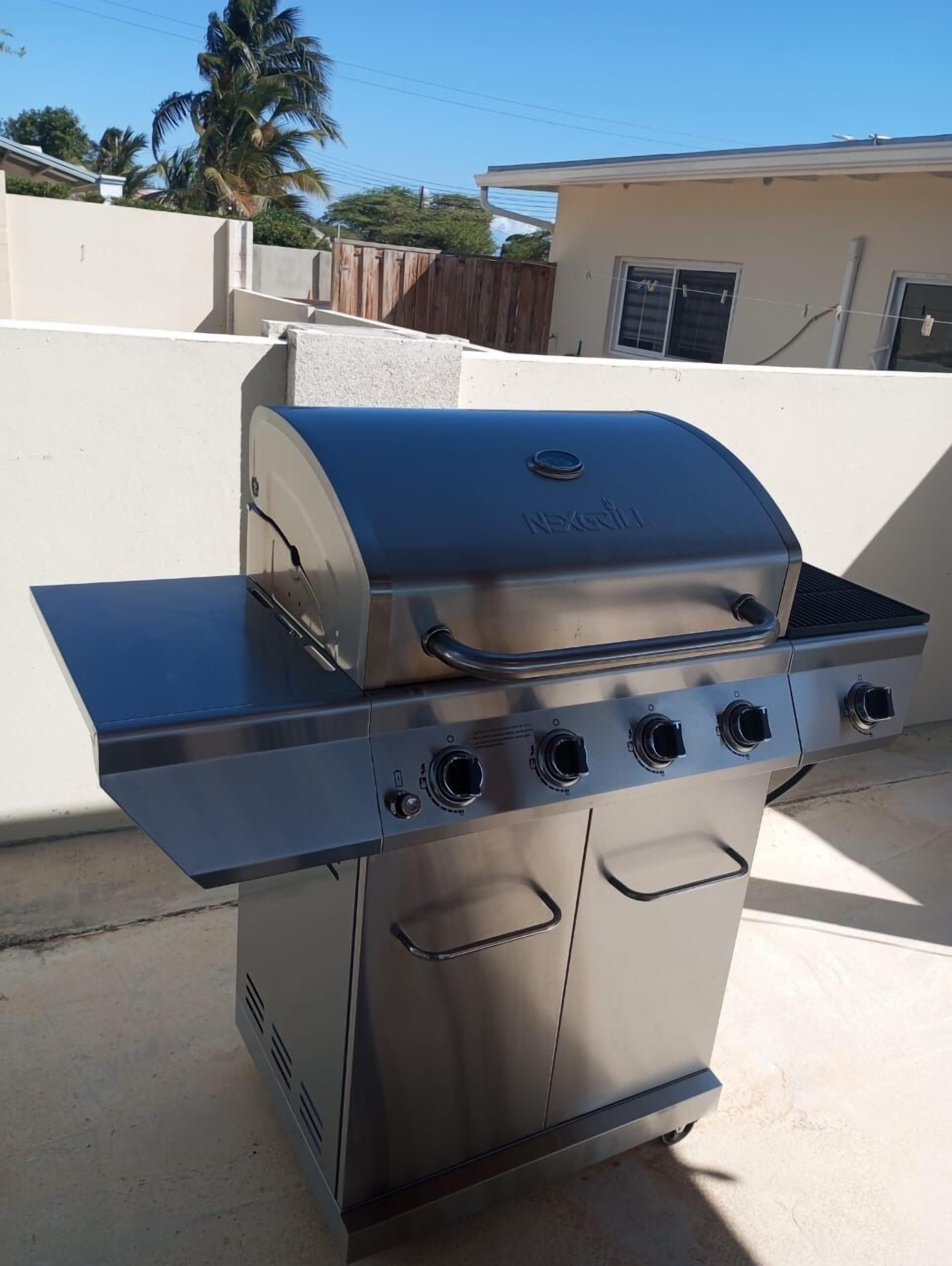 A stainless steel outdoor grill with four burners and a side shelf, located in a residential outdoor area.