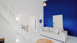 Un saló modern amb un sofà blanc, una paret d'accent blau i una escala.