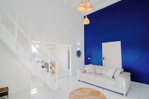 A modern living room with a white sofa, a blue accent wall, and a staircase.