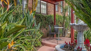 A patio with a table and chairs, surrounded by lush greenery and a stone fountain. - 2br Deluxe w/ Balcony in Historic Hotel San Diego (San Diego)