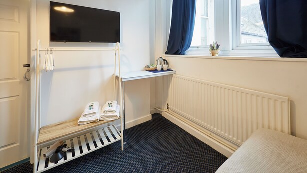 Hotelkamer met een bed, een aan de muur bevestigde televisie, een raam met gordijnen, een radiator en een plank met handdoeken en toiletartikelen.