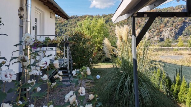 Un giardino con fiori bianchi, una struttura metallica e vista su un lago e delle colline.