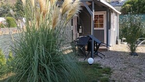 Una piccola struttura in legno con un portico coperto, circondata da erba alta e un vialetto sterrato.