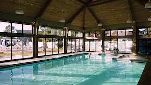 Une piscine intérieure avec de grandes baies vitrées, un plafond en bois et une vue sur l’extérieur.